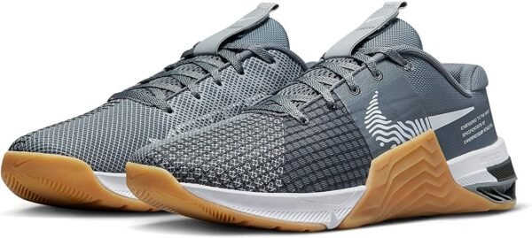 La imagen muestra un par de zapatillas de entrenamiento NIKE Metcon 8 en color gris y blanco con detalles en gris oscuro. Estas zapatillas son ideales para el entrenamiento de alta intensidad, CrossFit y levantamiento de pesas, con una suela resistente y una parte superior de malla transpirable para una mayor comodidad y soporte.